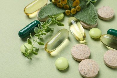 Photo of Different pills and herbs on light green background, closeup. Dietary supplements