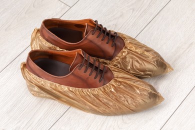 Photo of Men`s shoes in shoe covers on light wooden floor