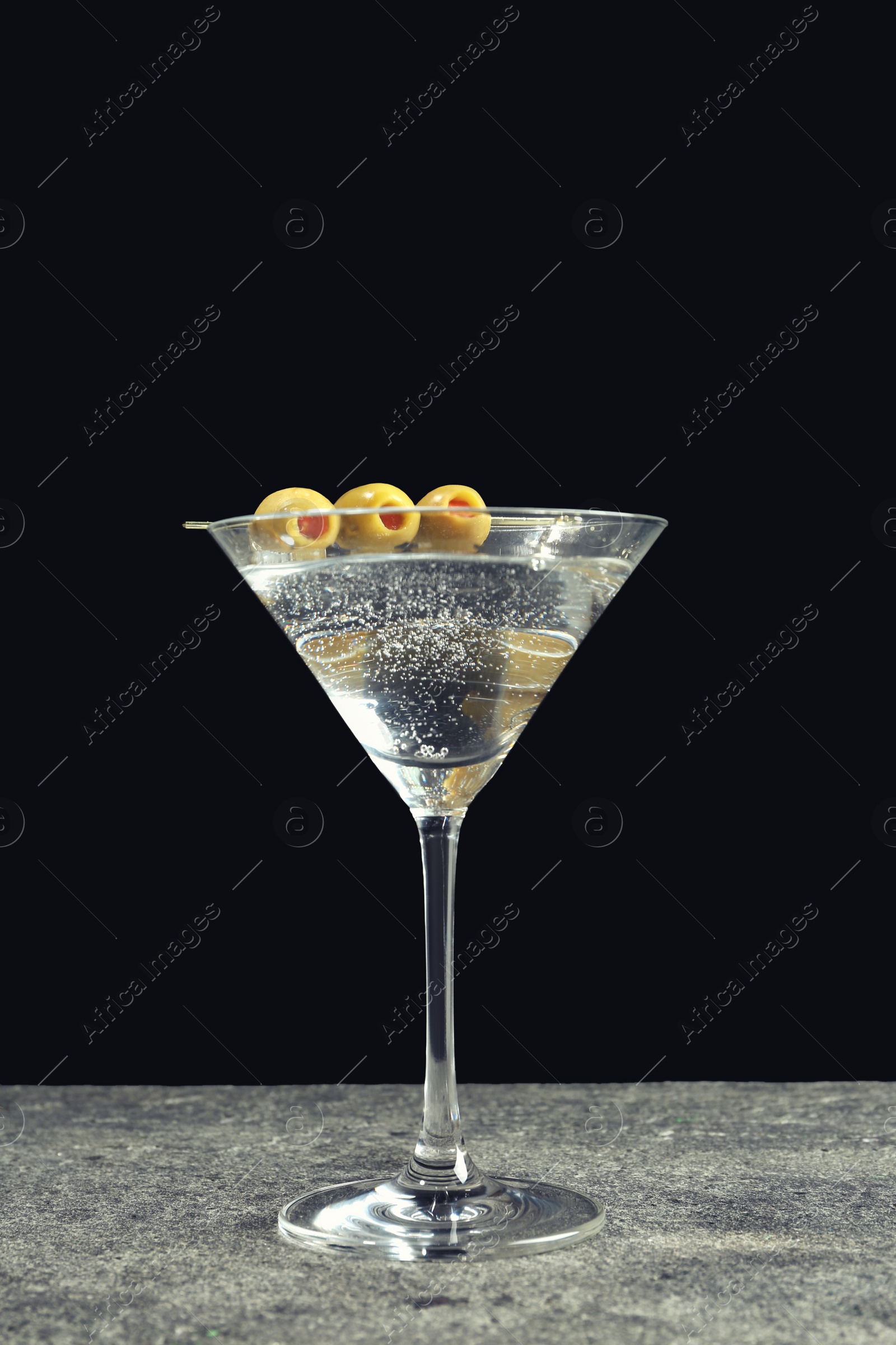 Photo of Martini cocktail with olives on grey table against dark background