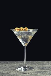 Photo of Martini cocktail with olives on grey table against dark background