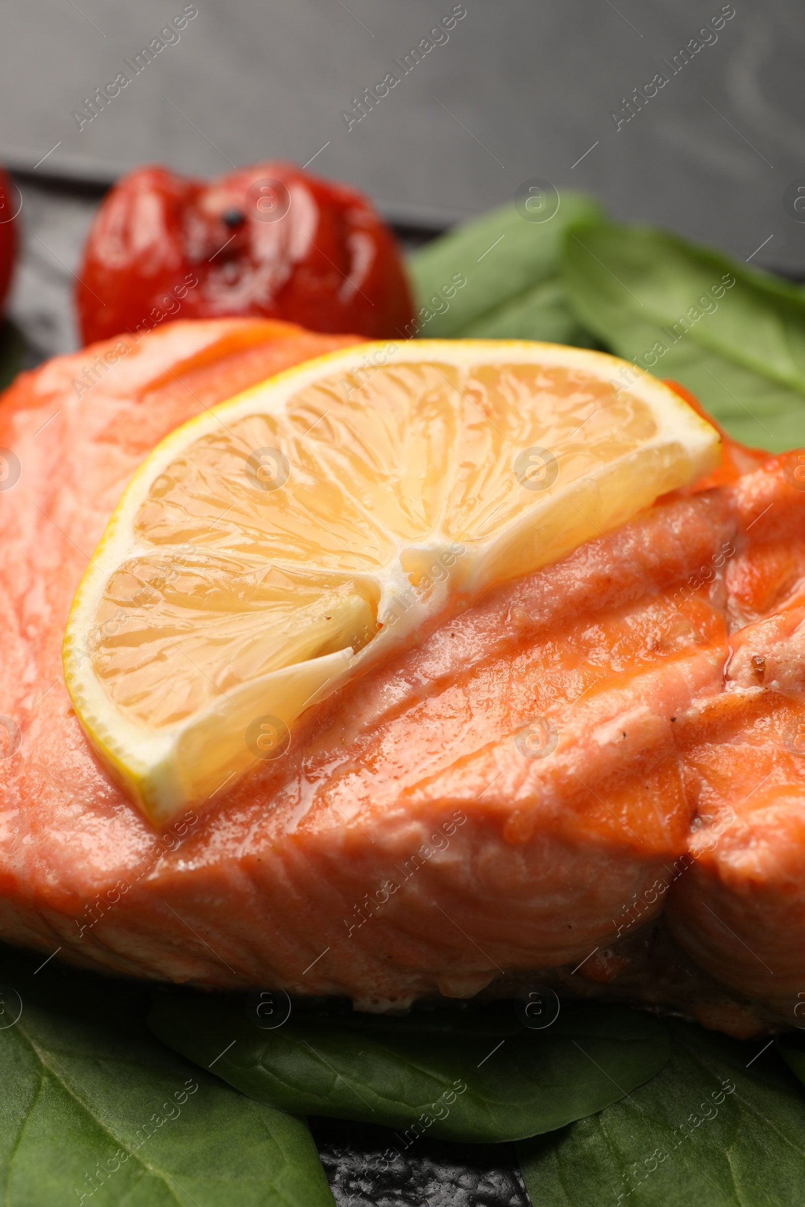 Photo of grilled salmon with tomato, spinach and lemon on table, closeup