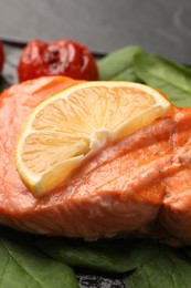 Photo of grilled salmon with tomato, spinach and lemon on table, closeup