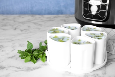 Photo of Cups of homemade fruit yogurt near multi cooker on marble table