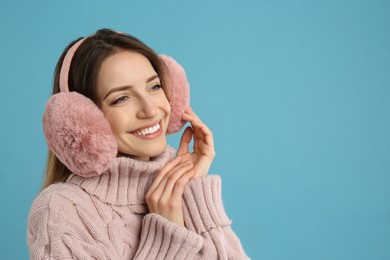 Photo of Happy woman wearing warm earmuffs on light blue background, space for text