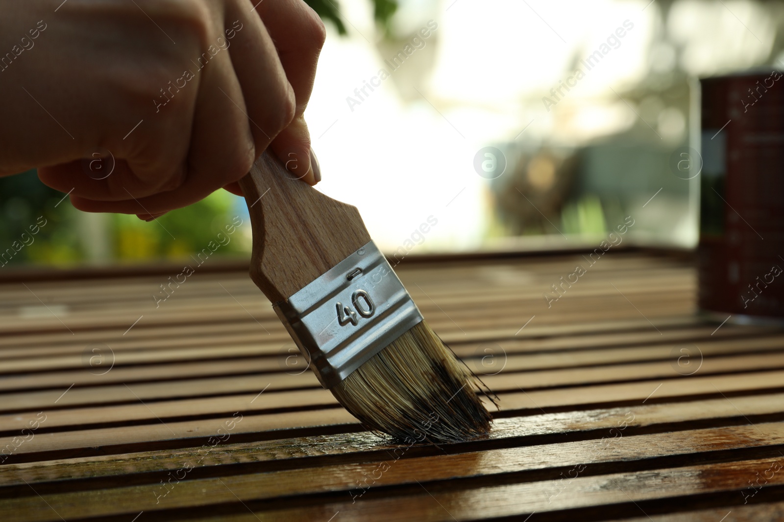Photo of Woman applying wood stain onto planks outdoors, closeup