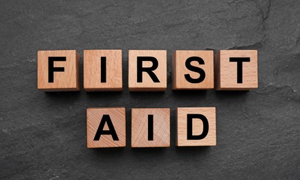 Words First Aid made of wooden cubes on black table, flat lay