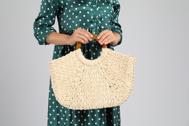 Photo of Young woman with stylish straw bag on light grey background, closeup