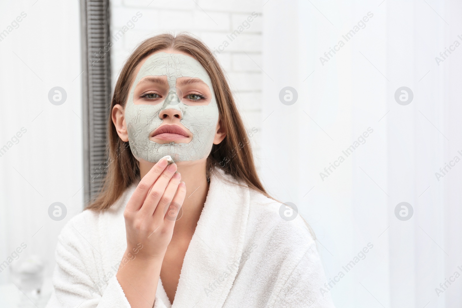 Photo of Beautiful woman removing clay mask from her face indoors