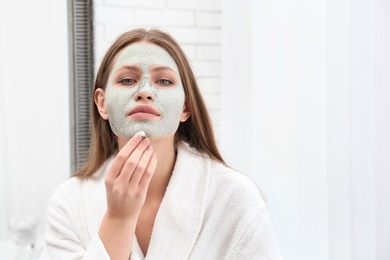 Beautiful woman removing clay mask from her face indoors
