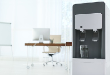 Photo of Modern water cooler with glass in office. Space for text