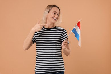 Photo of Happy woman pointing at flag of Netherlands on beige background