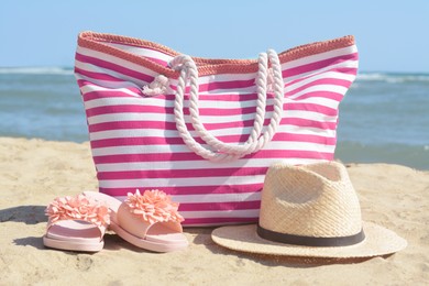 Photo of Stylish striped bag with straw hat and slippers on sandy beach near sea