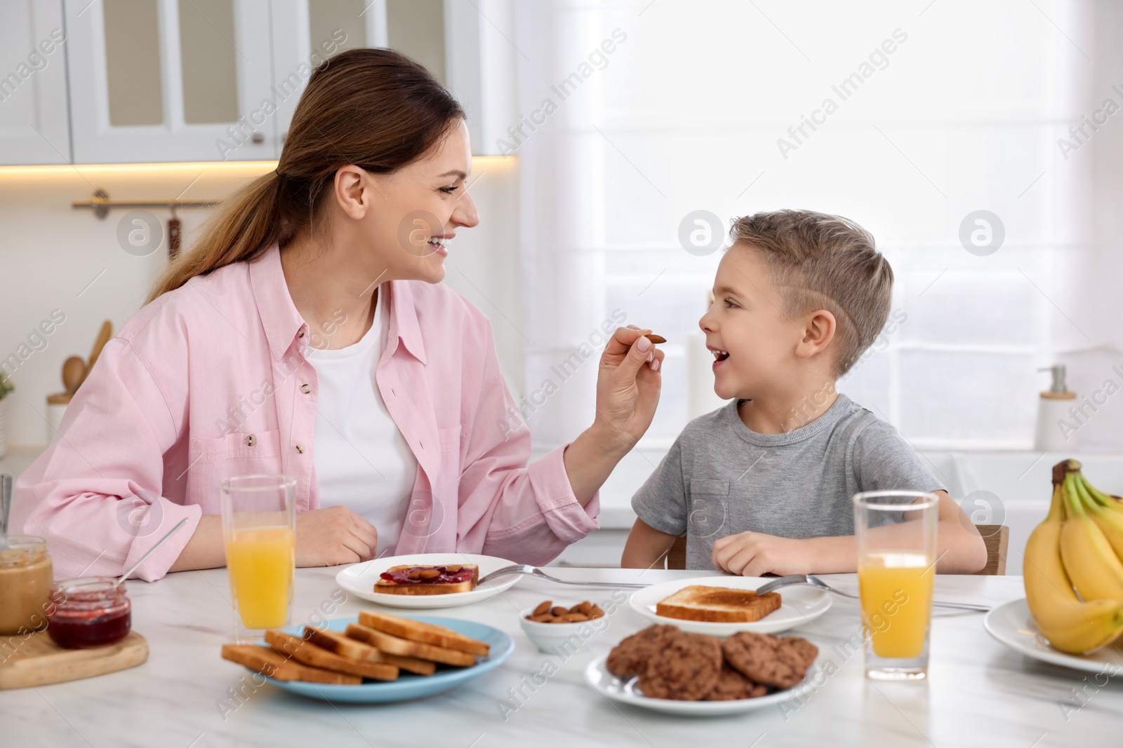 Photo of Mother and her cute little son having breakfast at table in kitchen