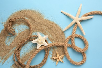 Photo of Beautiful sea stars, rope and sand on light blue background, flat lay