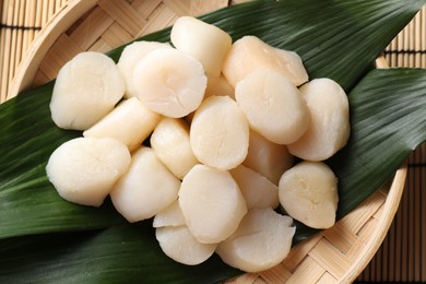 Fresh raw scallops in bowl on bamboo mat, top view