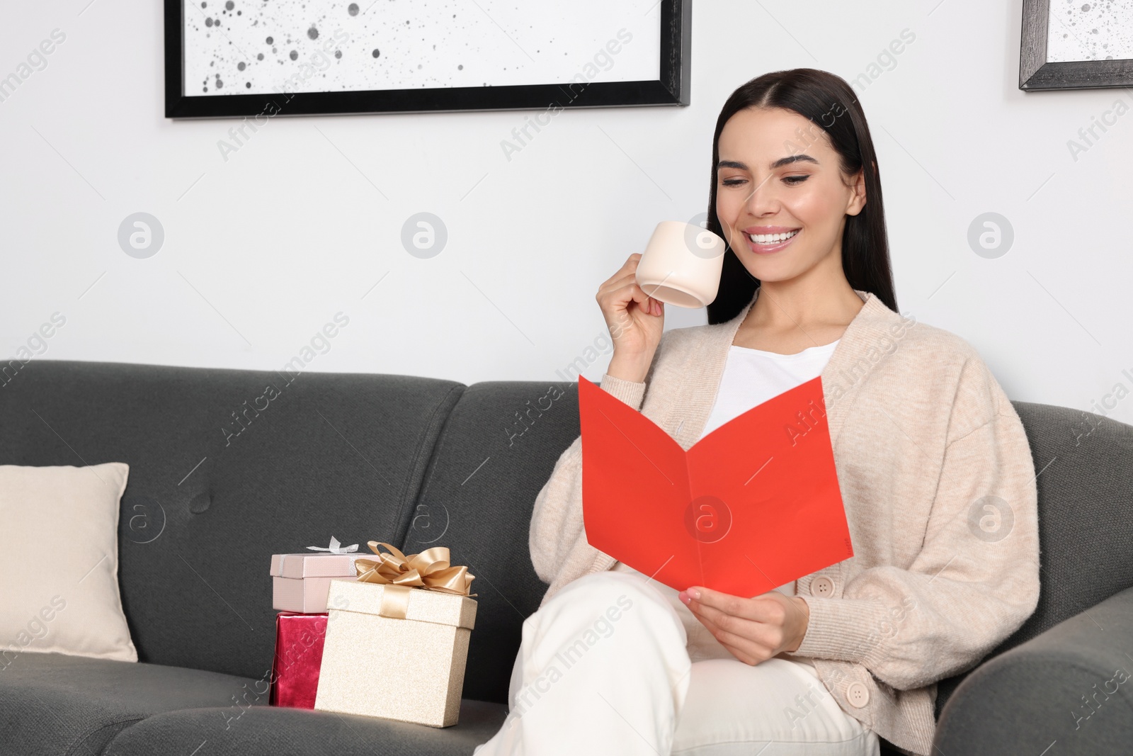 Photo of Happy woman reading greeting card while drinking coffee on sofa in living room