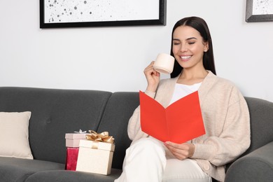 Happy woman reading greeting card while drinking coffee on sofa in living room