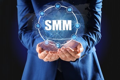 Image of Social media marketing concept. Man holding virtual icon SMM in hands on dark background, closeup