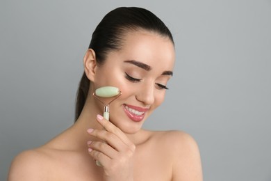 Photo of Woman using natural jade face roller on grey background