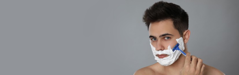 Image of Handsome young man shaving with razor on grey background, space for text. Banner design