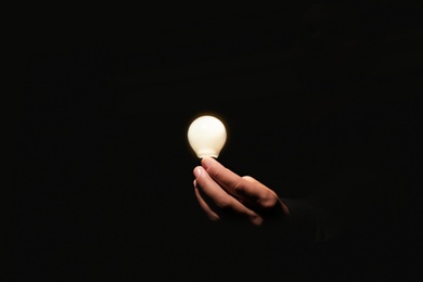 Man holding modern lamp bulb on dark background, closeup