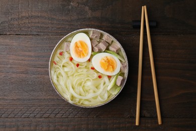 Photo of Bowl of delicious rice noodle soup with meat and egg on wooden table, flat lay