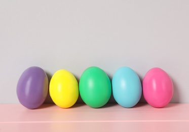 Easter eggs on pink wooden table against light grey background, space for text