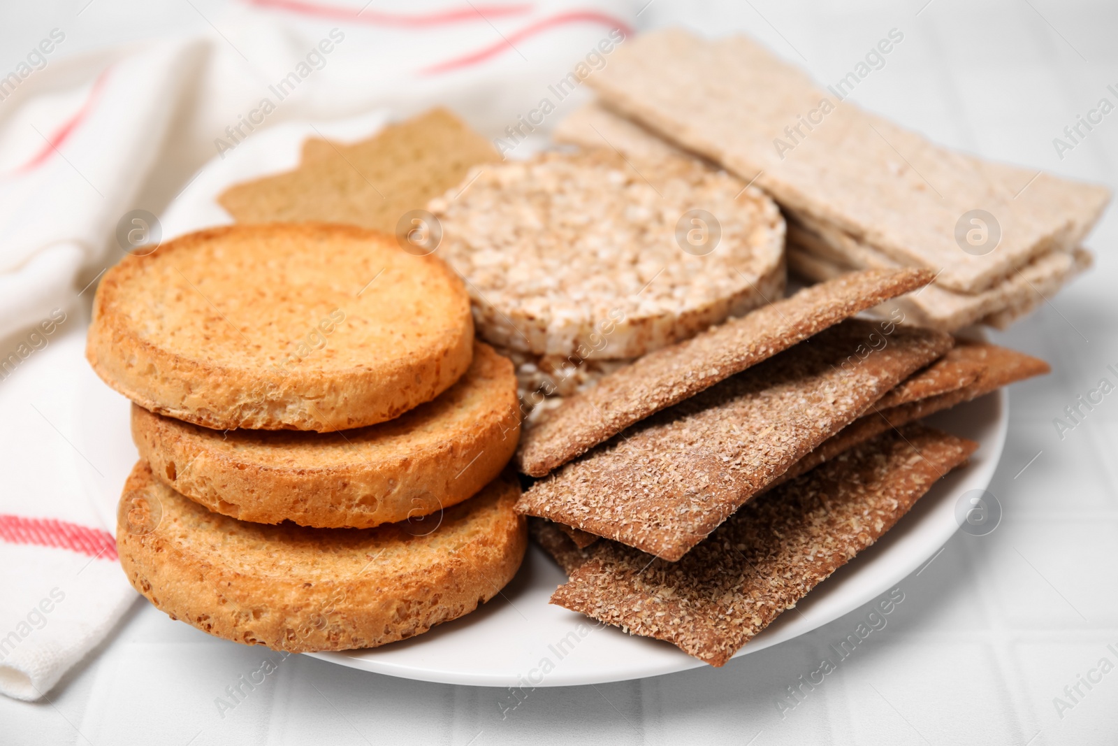 Photo of Plate of rye crispbreads, rice cakes and rusks on white checkered table