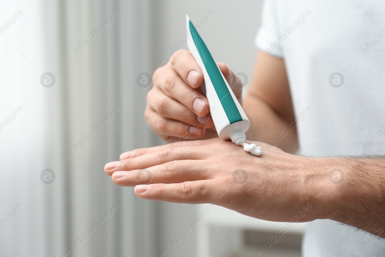 Photo of Man applying cream from tube onto hand indoors, closeup