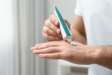 Man applying cream from tube onto hand indoors, closeup