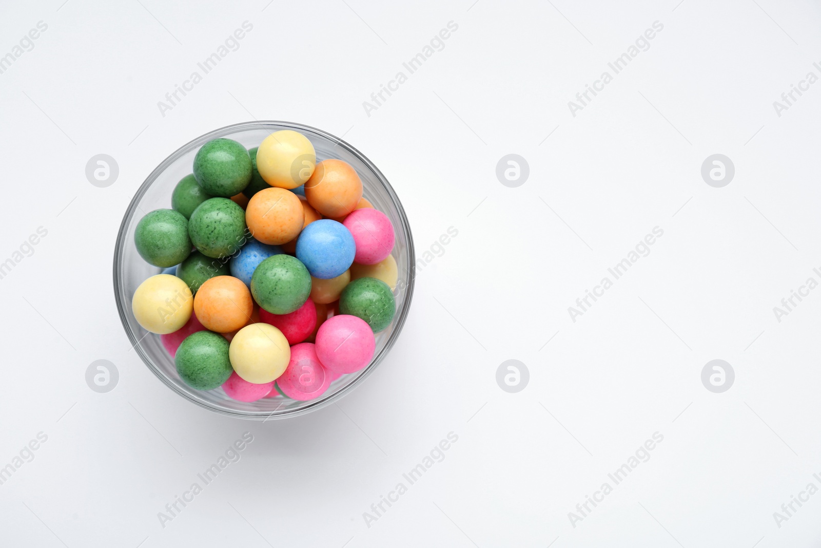Photo of Bowl with many bright gumballs on white background, top view. Space for text