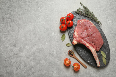 Photo of Raw rib with herbs, spices and tomatoes on grey table, flat lay. Space for text