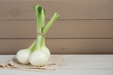 Bunch of fresh green spring onions on white wooden table, space for text
