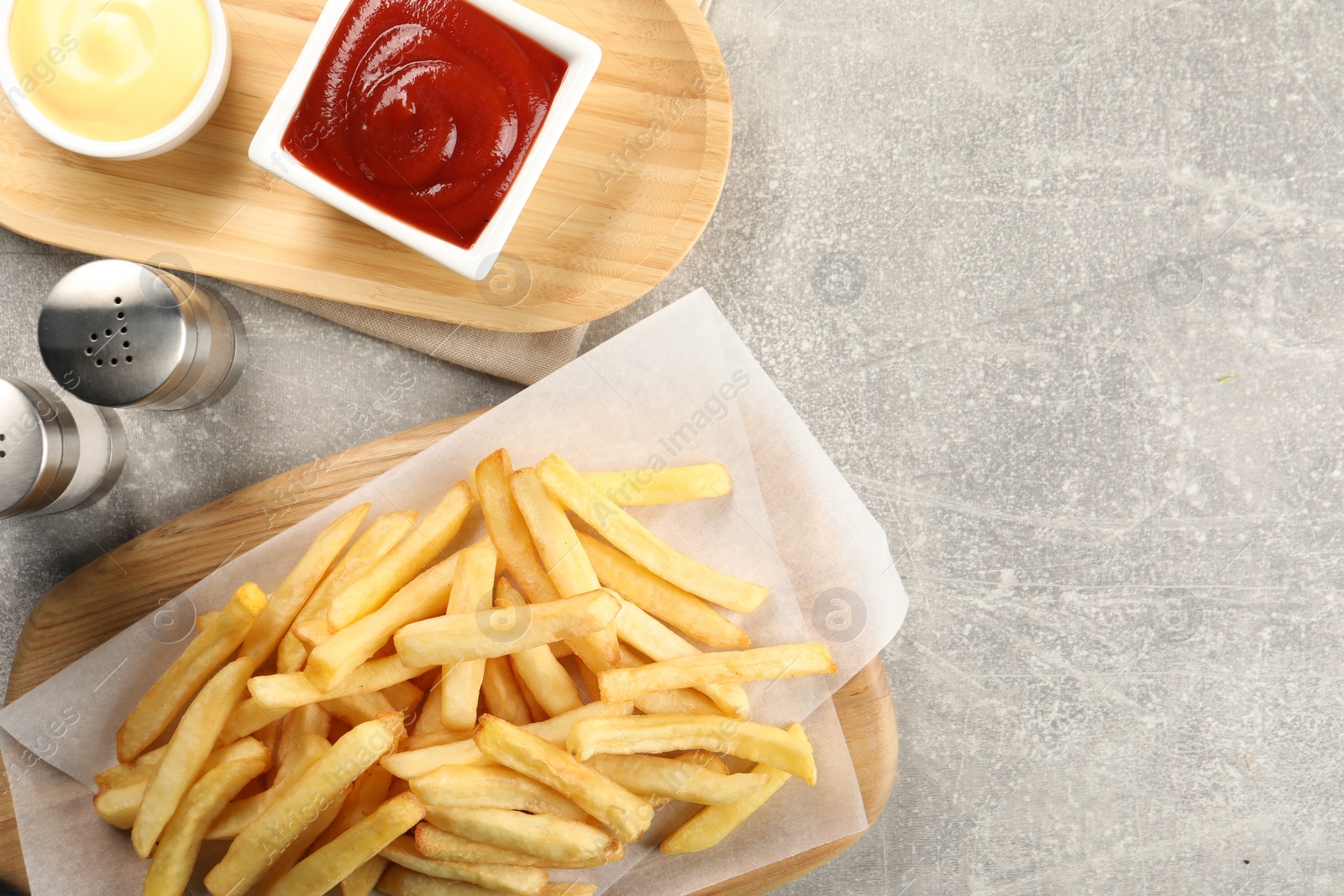 Photo of Delicious french fries served with sauces on light grey table, flat lay. Space for text