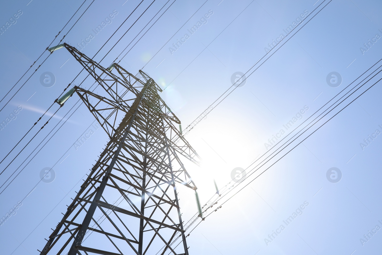 Photo of High voltage tower with electricity transmission power lines against blue sky, low angle view