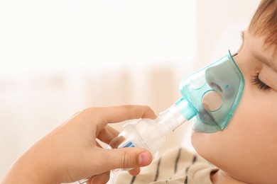 Boy using nebulizer for inhalation on blurred background, closeup