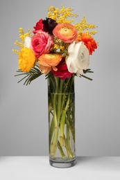 Photo of Vase with beautiful ranunculus and mimosa flowers on light background