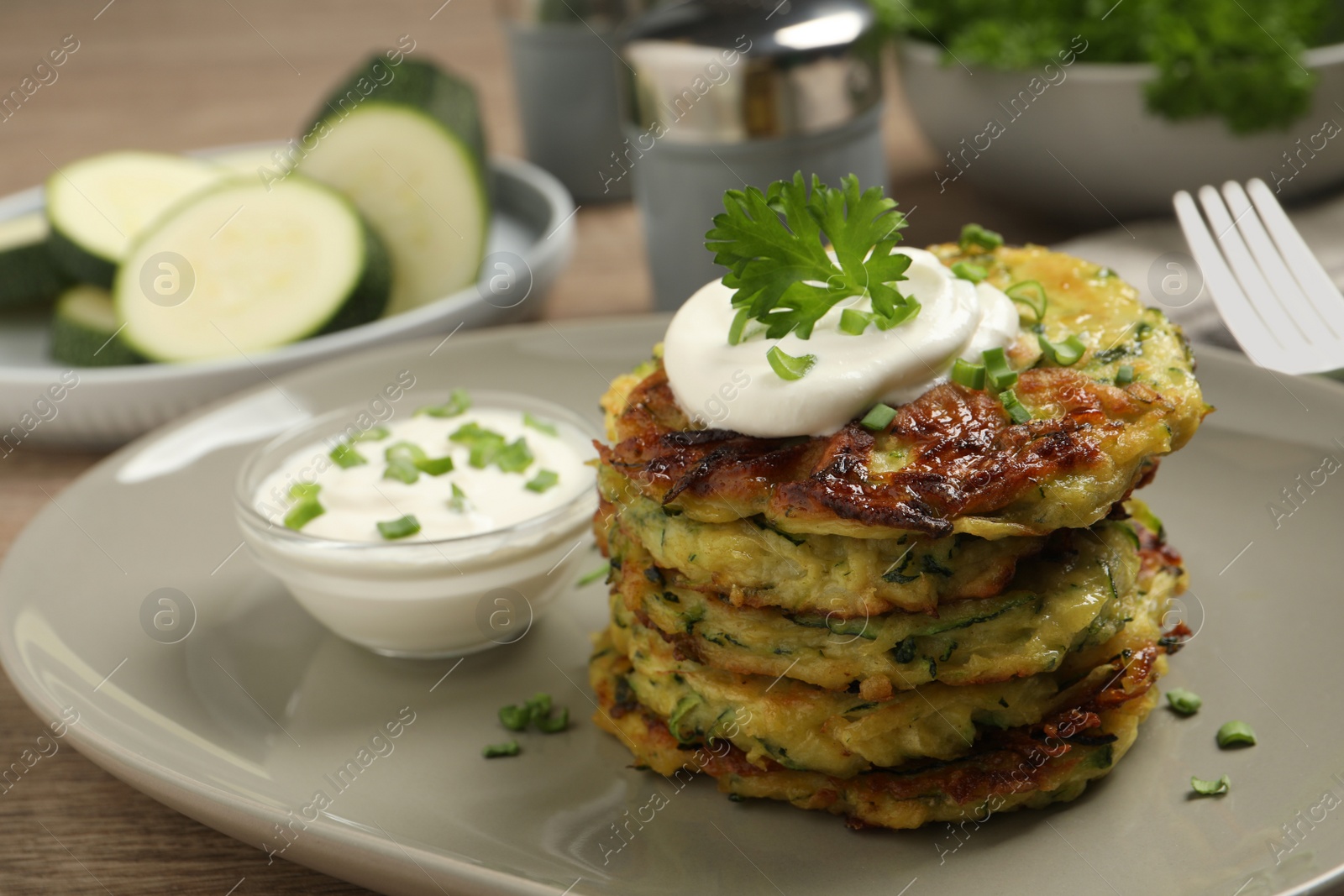 Photo of Delicious zucchini fritters with sour cream served on table, closeup