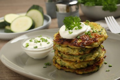 Photo of Delicious zucchini fritters with sour cream served on table, closeup