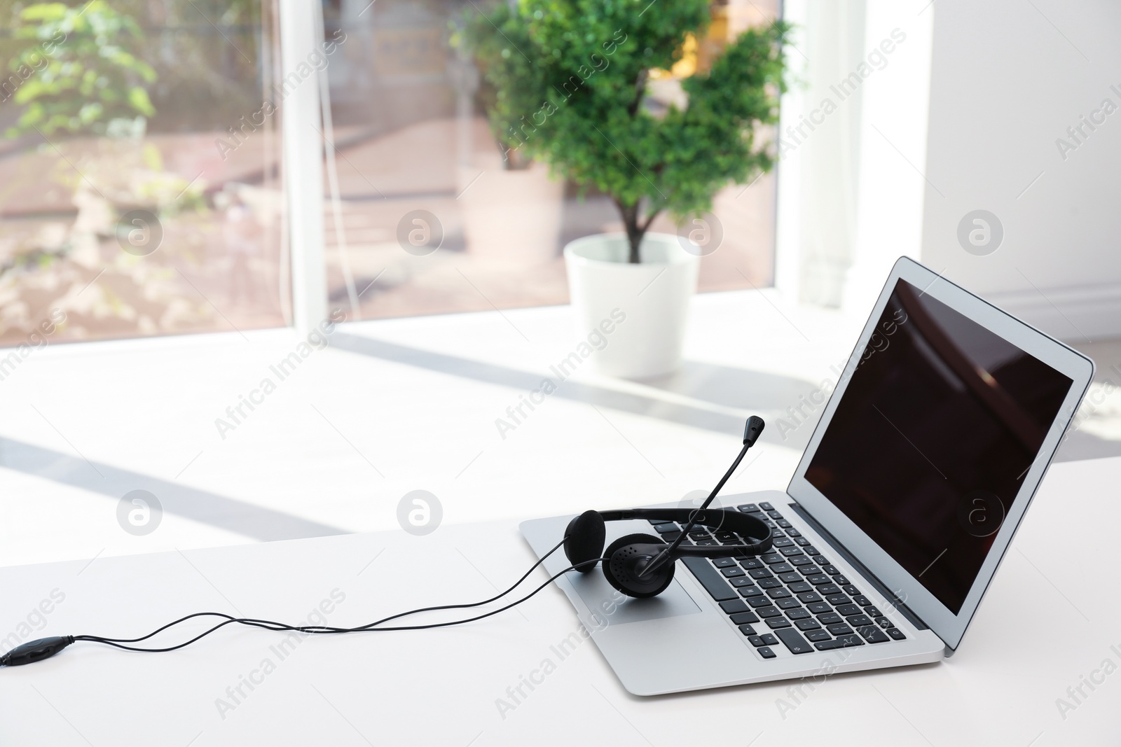 Photo of Modern laptop and headset on table indoors. Technical support concept