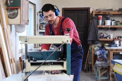 Photo of Mature working man using thickness planer at carpentry shop