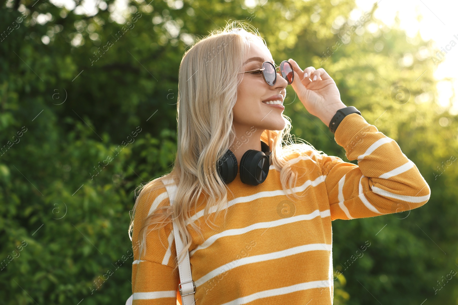 Photo of Portrait of happy young woman with headphones in park on spring day