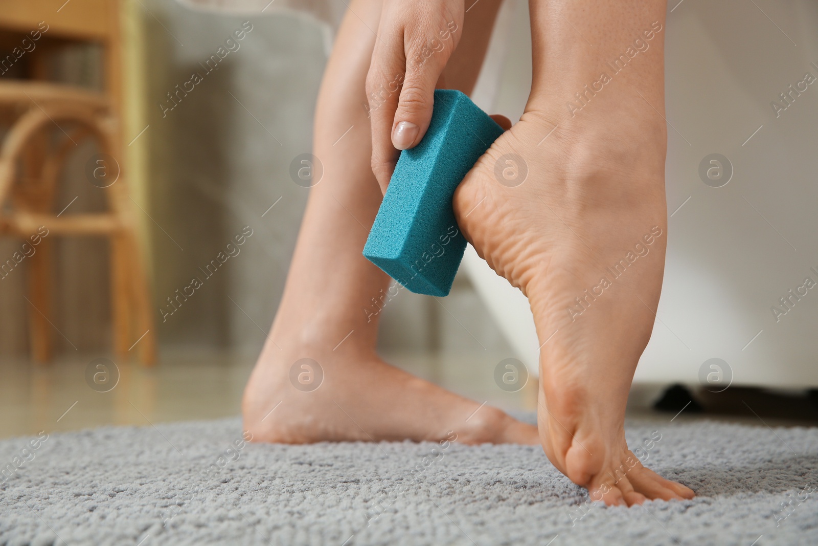 Photo of Woman using pumice stone for removing dead skin from feet indoors, closeup