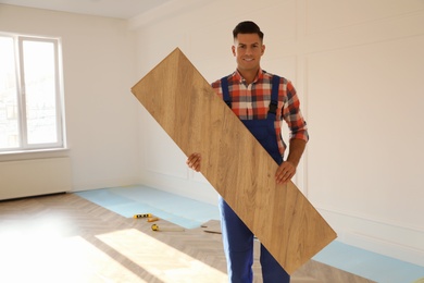 Photo of Professional worker with wooden board indoors. Installing of parquet flooring