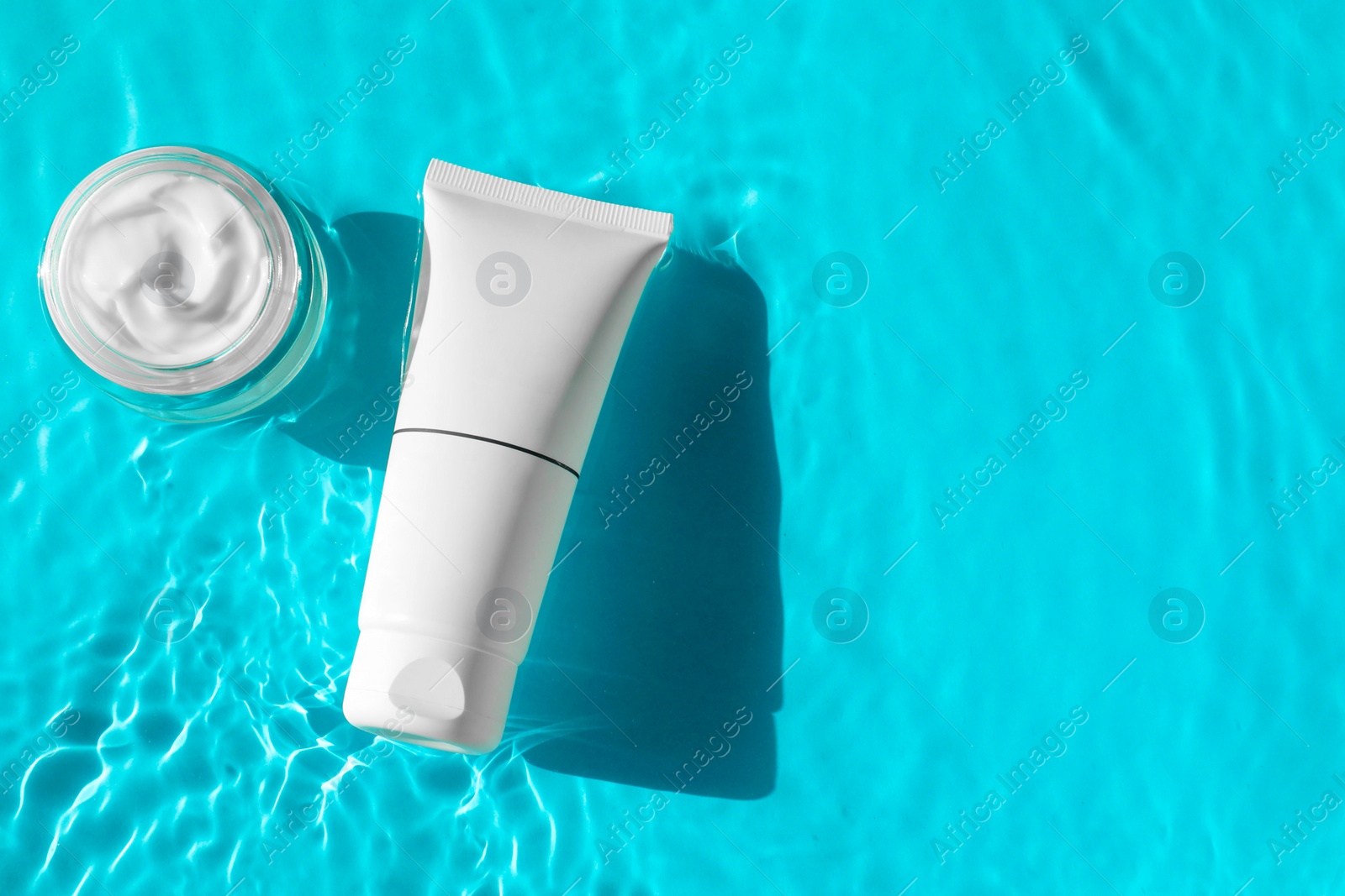 Photo of Tube and jar with moisturizing cream in water on light blue background, top view. Space for text