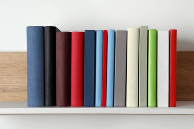 Photo of Many hardcover books on wooden shelf near white wall