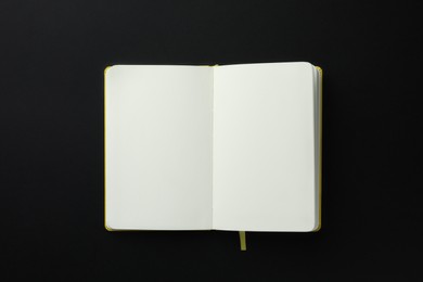 Open notebook with blank pages on black background, top view. Space for text