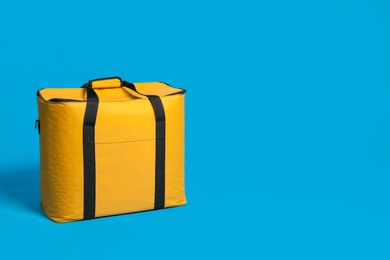 Photo of Modern yellow thermo bag on light blue background. Space for text