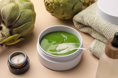 Photo of Package of under eye patches, cosmetic products and artichokes on beige background, closeup