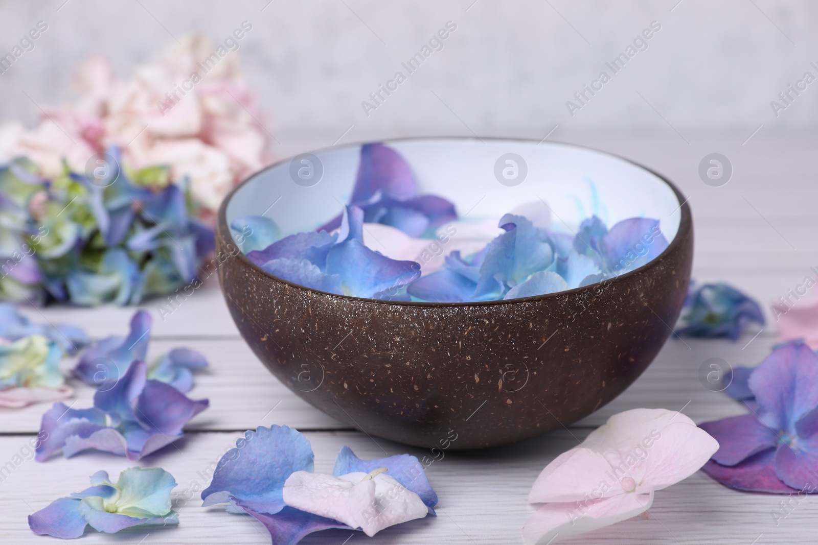 Photo of Spa composition. Aromatic water in bowl and flowers on white wooden table, closeup